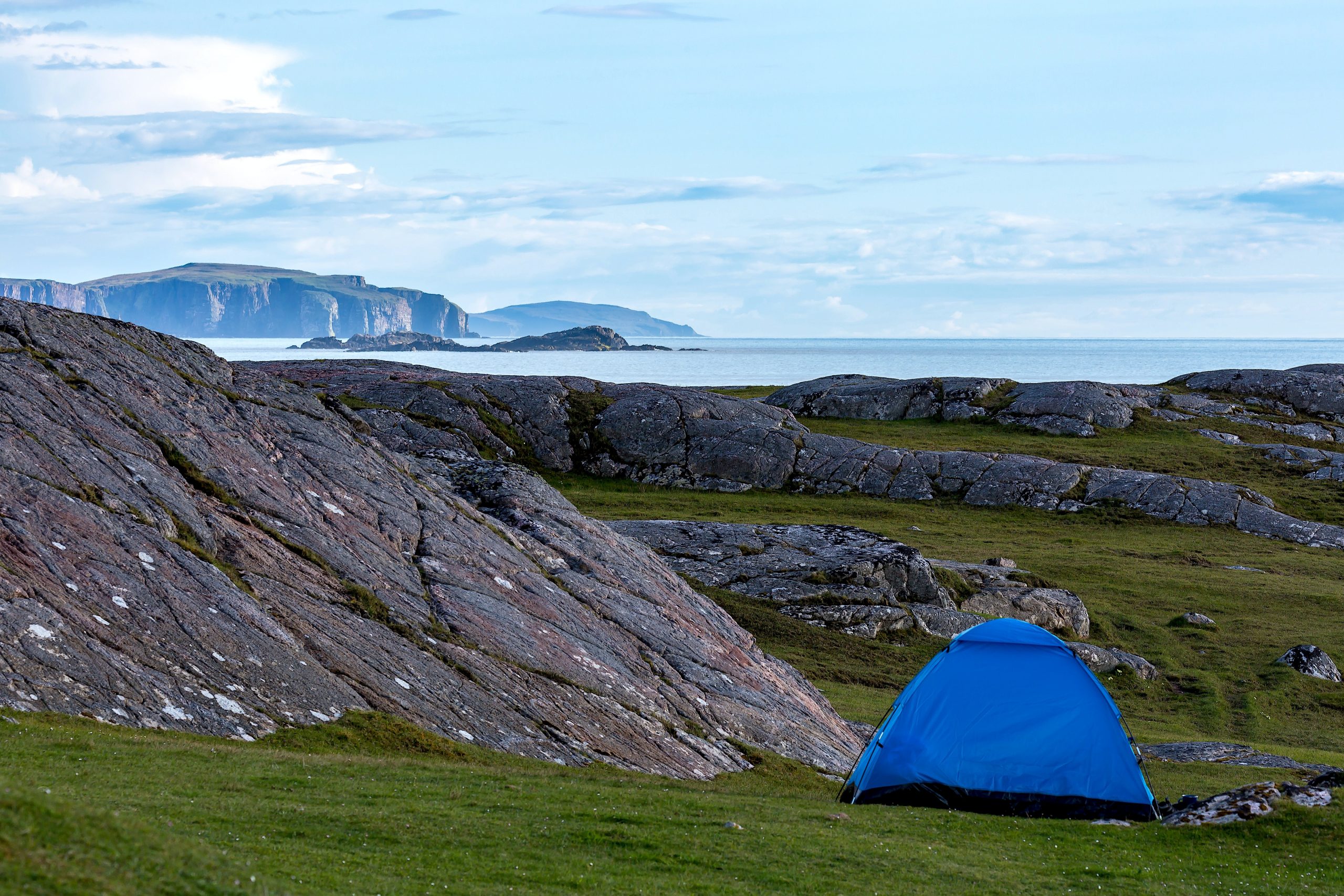 blue dome tent on green grass field near mountain under white clouds during daytime